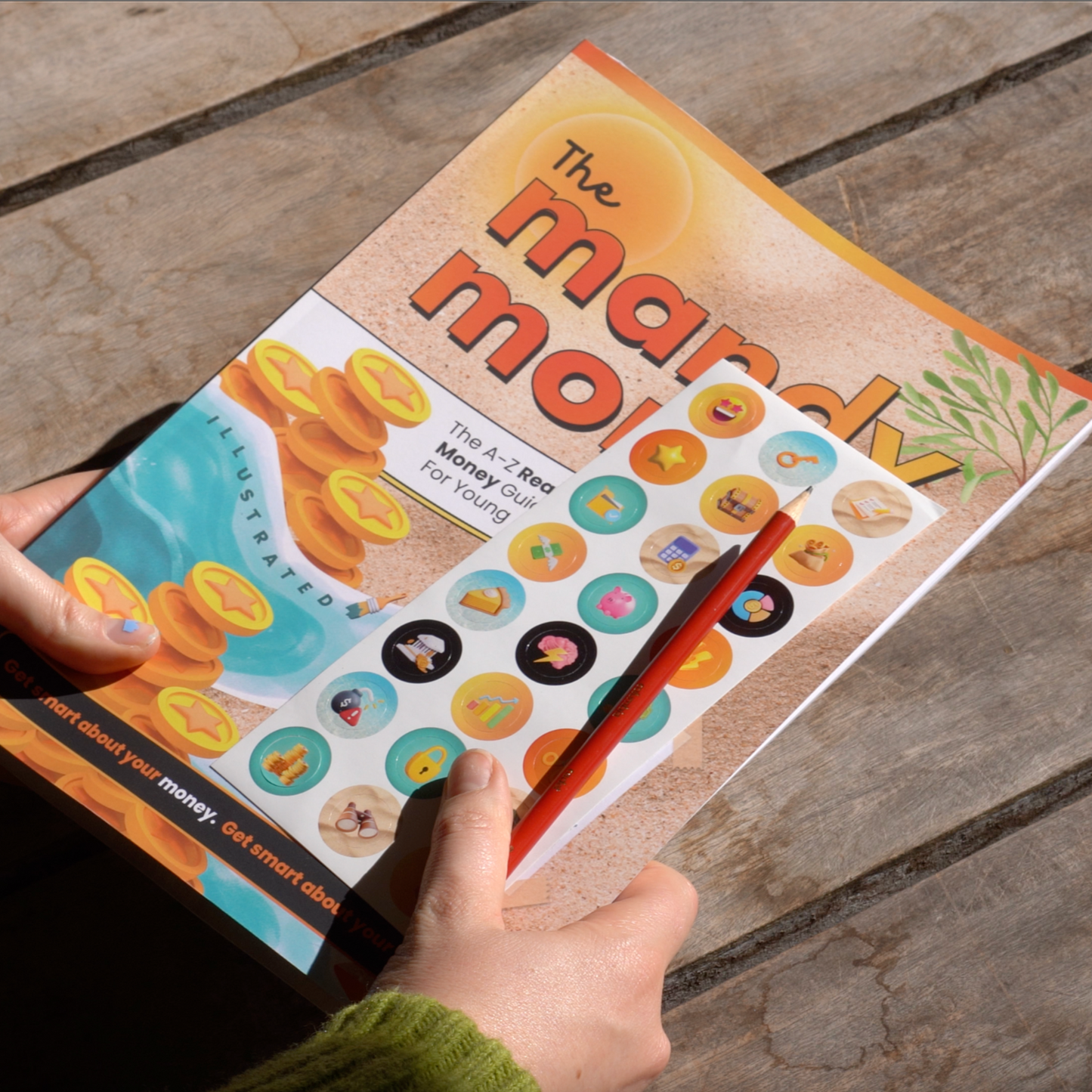 Person holding a book titled 'The mandy money book' the all-in-one ✨illustrated✨ roadmap for aussie teenagers to transitioning into the real world of money