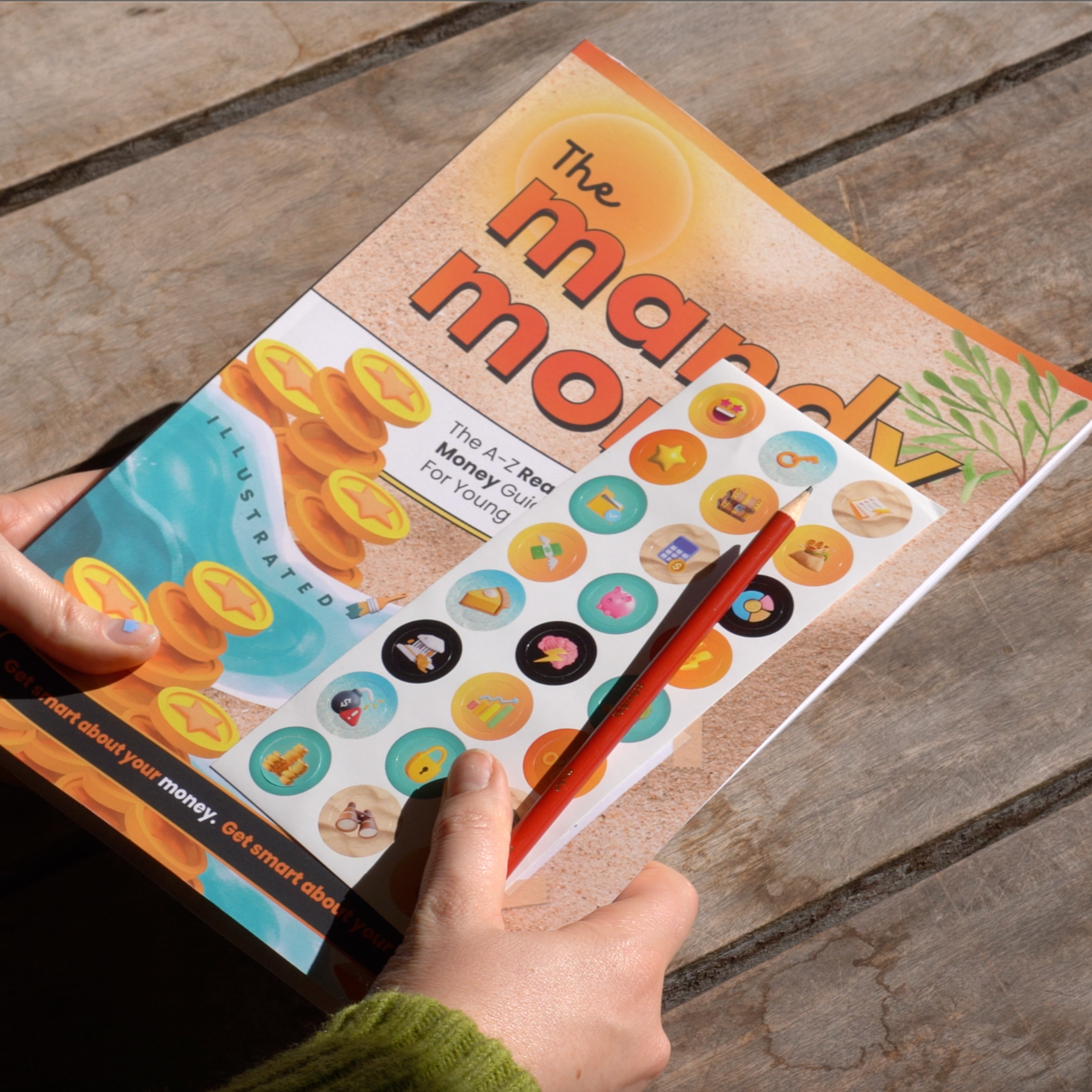Person holding a book titled 'The mandy money book' the all-in-one ✨illustrated✨ roadmap for aussie teenagers to transitioning into the real world of money